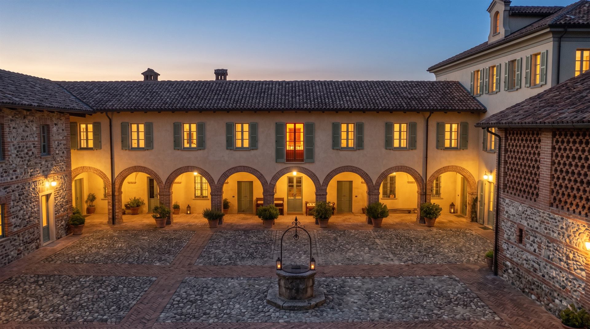 La corte della cascina la sera, con il pozzo e il portico ad archi illuminato